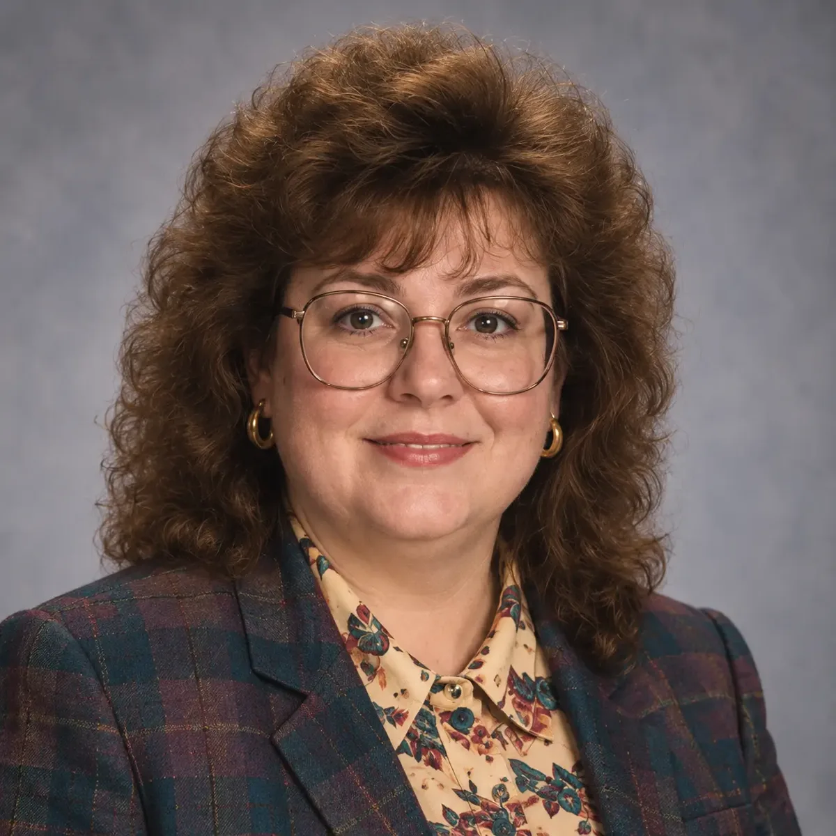 Portrait of Gertrude in glasses, a plaid blazer and floral blouse.